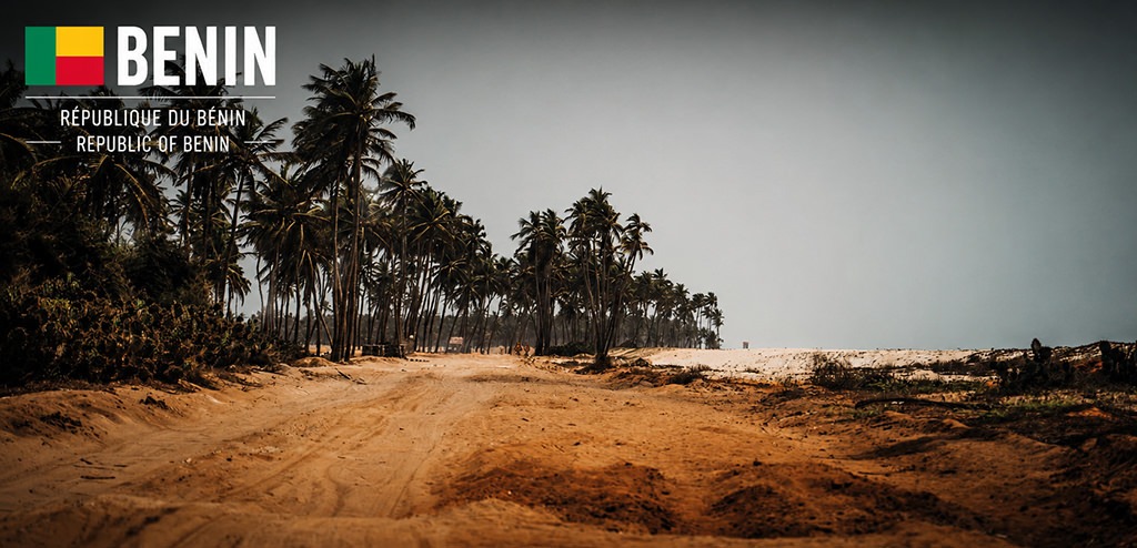 Cinematic coastal landscape in Benin featuring a sandy dirt track lined with palm trees along the Atlantic Ocean. The travel poster includes the Benin flag, country name and official country designation in French and English.