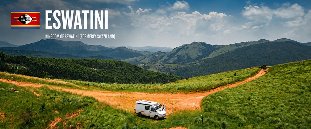 White overland camper parked beside a dirt road in the green hills of Eswatini, surrounded by rolling mountains and lush grasslands under a blue sky.