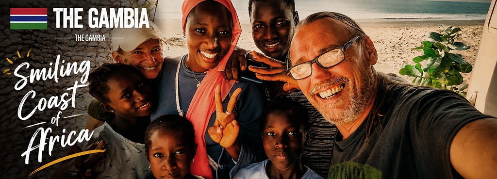 Fenny and Totti posing with a Gambian family on a beach in The Gambia, sharing smiles during a spontaneous encounter while overlanding across Africa.