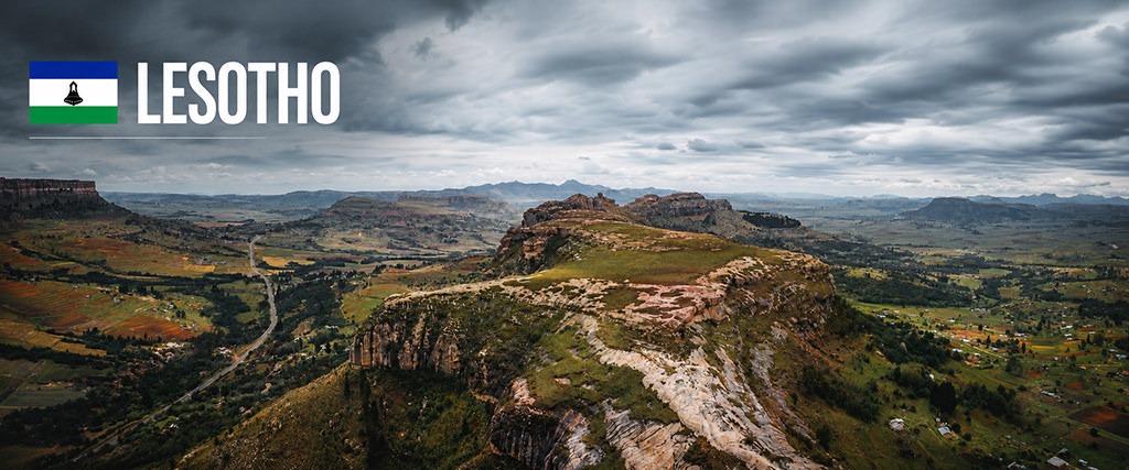 Panoramic view of the mountainous landscapes of Lesotho under dramatic storm clouds, featuring rocky plateaus, green valleys and scattered villages.