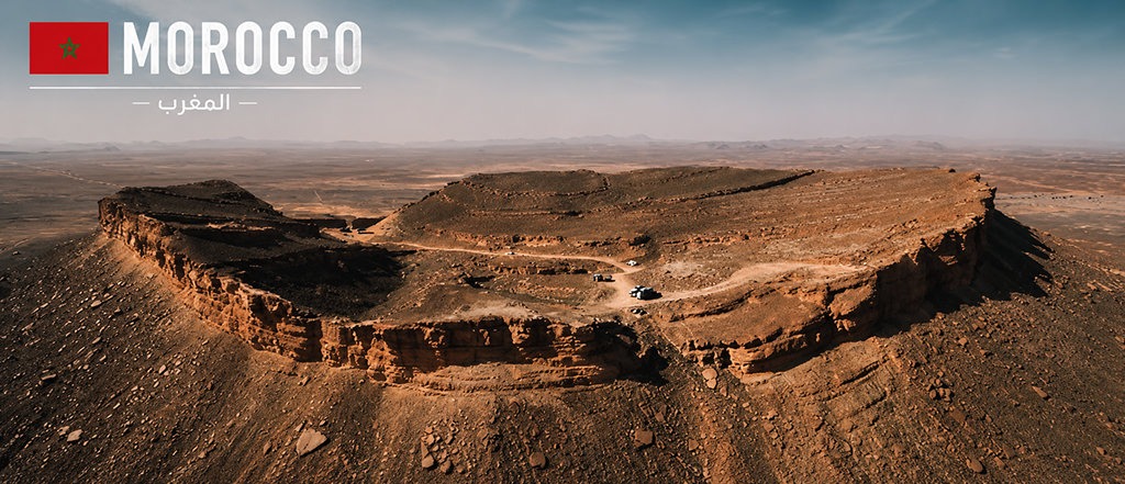 Aerial view of the Medouar Crater in southeastern Morocco, a massive horseshoe-shaped rock formation surrounded by desert landscapes.