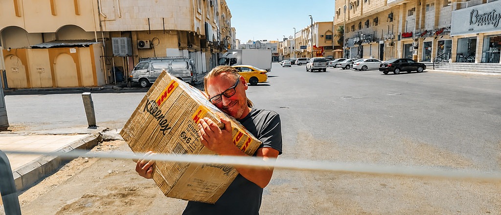 Happy overlander hugging a DHL Express parcel after successful delivery during an overland journey through the Middle East.