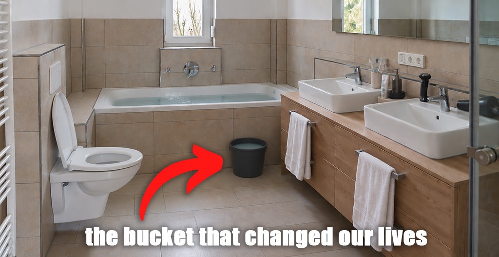 Bathroom with a bathtub, toilet and bucket of reused bathwater, illustrating a water-saving habit