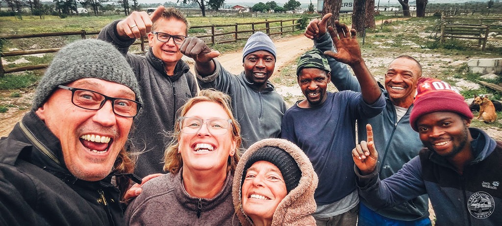A group of travellers and mechanics smiling together after successfully loading their vehicles into shipping containers in South Africa.