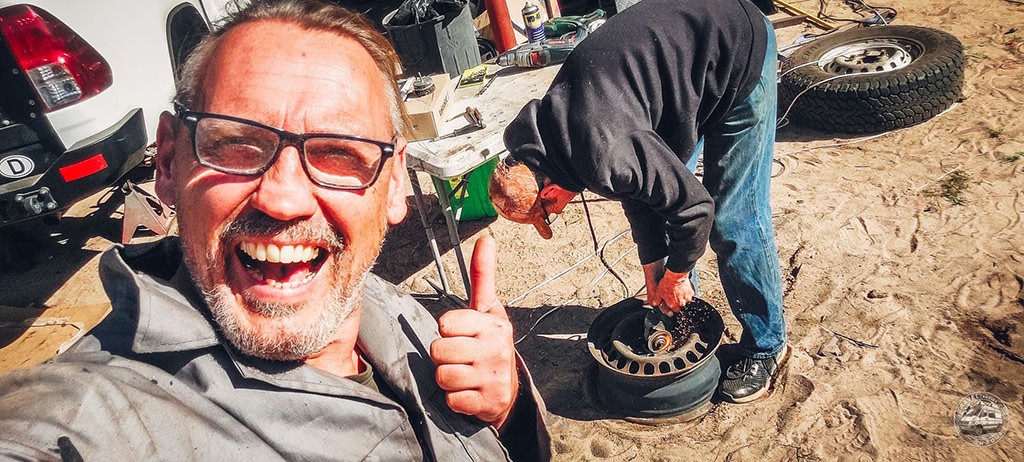Totti smiling and giving a thumbs-up while a mechanic works on a wheel to prepare special container rims for the Mercedes Sprinter. Title